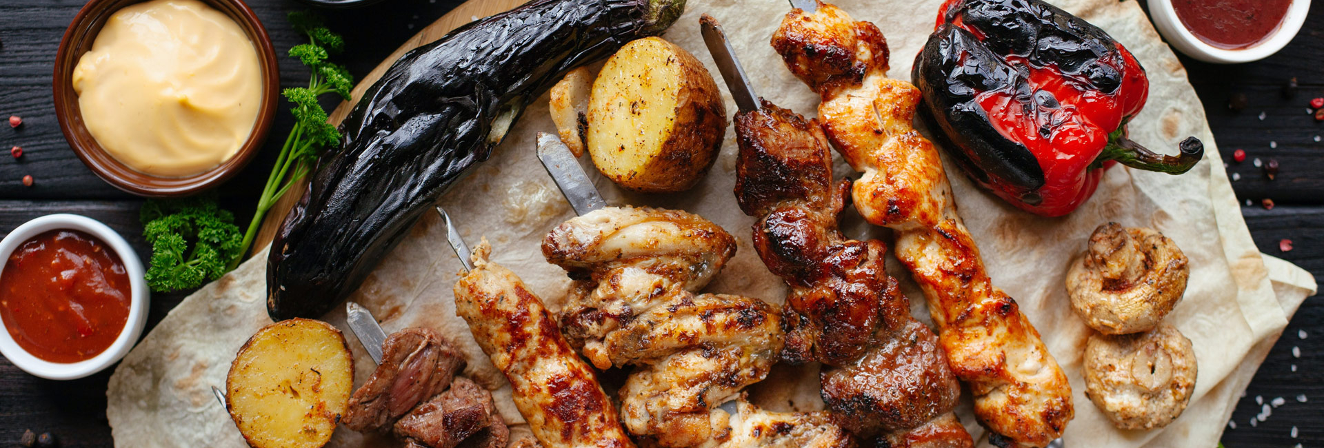 Various grilled meat including chicken and beef kebabs, potatoes, a red pepper and aubergine.