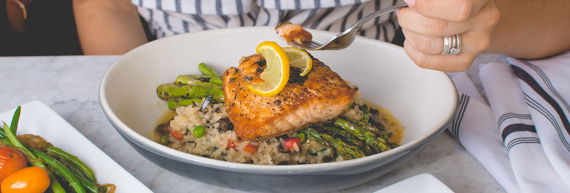 Lady diner eating grilled fish, asparagus, and rice with peas.