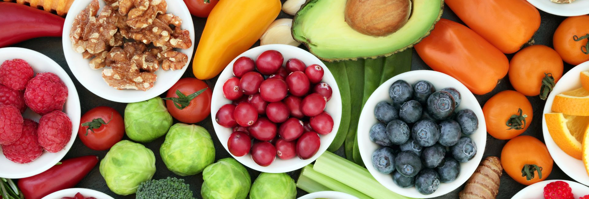 Fresh fruit and vegetables in bowls and on a table, along with some nuts.