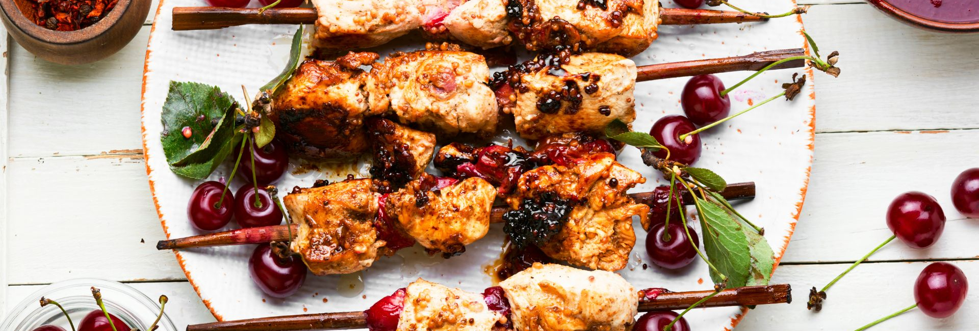 Marinated chicken sosaties on white plate with cherries