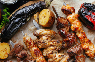 Various grilled meat including chicken and beef kebabs, potatoes, a red pepper and aubergine.