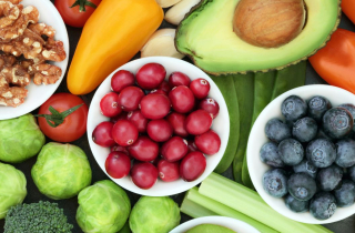 Fresh fruit and vegetables in bowls and on a table, along with some nuts.