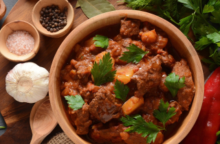 Pot of goulash surrounded by herbs and spices