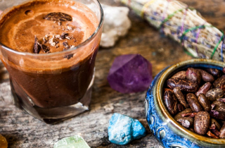 Cacao beans in blue bowl next to glass of cacao.