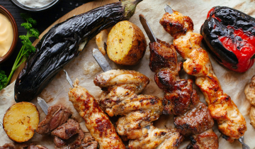 Various grilled meat including chicken and beef kebabs, potatoes, a red pepper and aubergine.