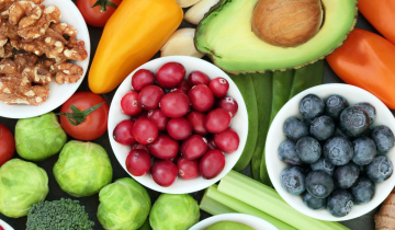 Fresh fruit and vegetables in bowls and on a table, along with some nuts.