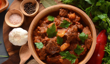Pot of goulash surrounded by herbs and spices